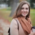 Kobieta w płaszczu z kubkiem kawy sfotografowana w parku