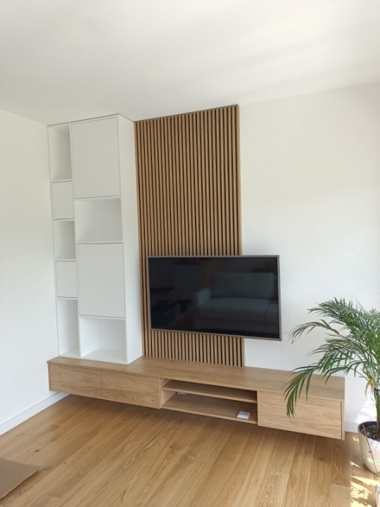 Drewniana wisząca szafka pod telewizorem oraz drewniana boazeria za telewizorem w salonie